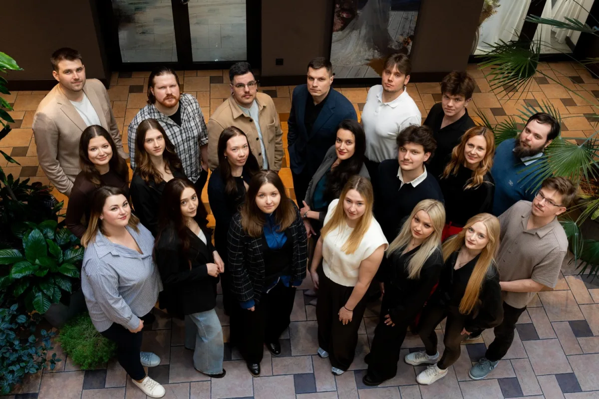 The eComCademy team standing together in a plant filled atrium, photographed from above and looking up at the camera
